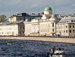 A row of large, stone three-story buildings alongside a large riverbank.