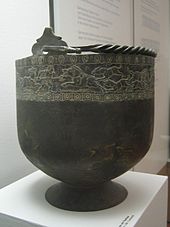 Large black bowl-shaped bucket on a stand. The bucket has incrustation around its top.