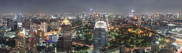 Night-time panorama photograph showing an expansive cityscape with several skyscrapers in the foreground, a park in the centre, and a large group of buildings across the park