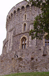 A photograph showing the left hand side of a circular stone tower made of grey stone and with small windows.