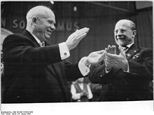 Two smiling men raise bouquets of flowers over their heads.