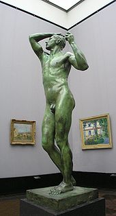 Life-sized nude stature of a male on a  pedestal on display in a museum.