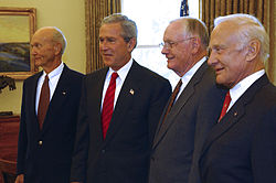 Photo of four men wearing suits, with the curtain drawn behind them, admitting light.