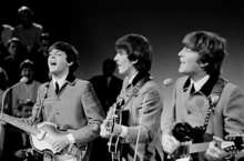 Paul McCartney, George Harrison, and John Lennon playing guitars and wearing matching grey suits.