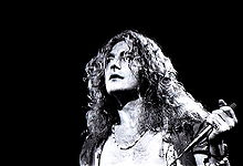 A black and white photograph showing a headshot of Robert Plant with a microphone in hand